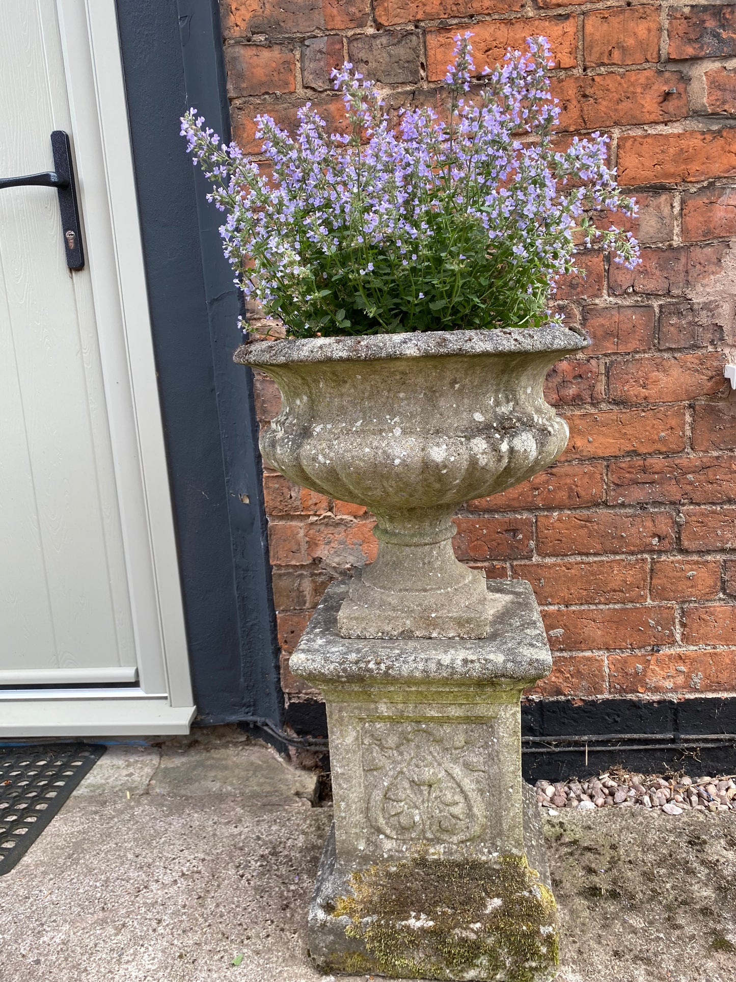 Decorative stone urn with flowers against a brick wall