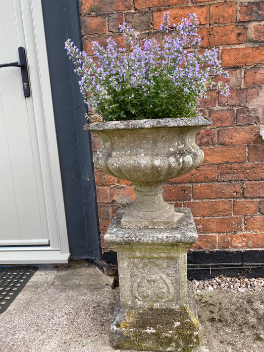 Decorative stone urn with flowers against a brick wall