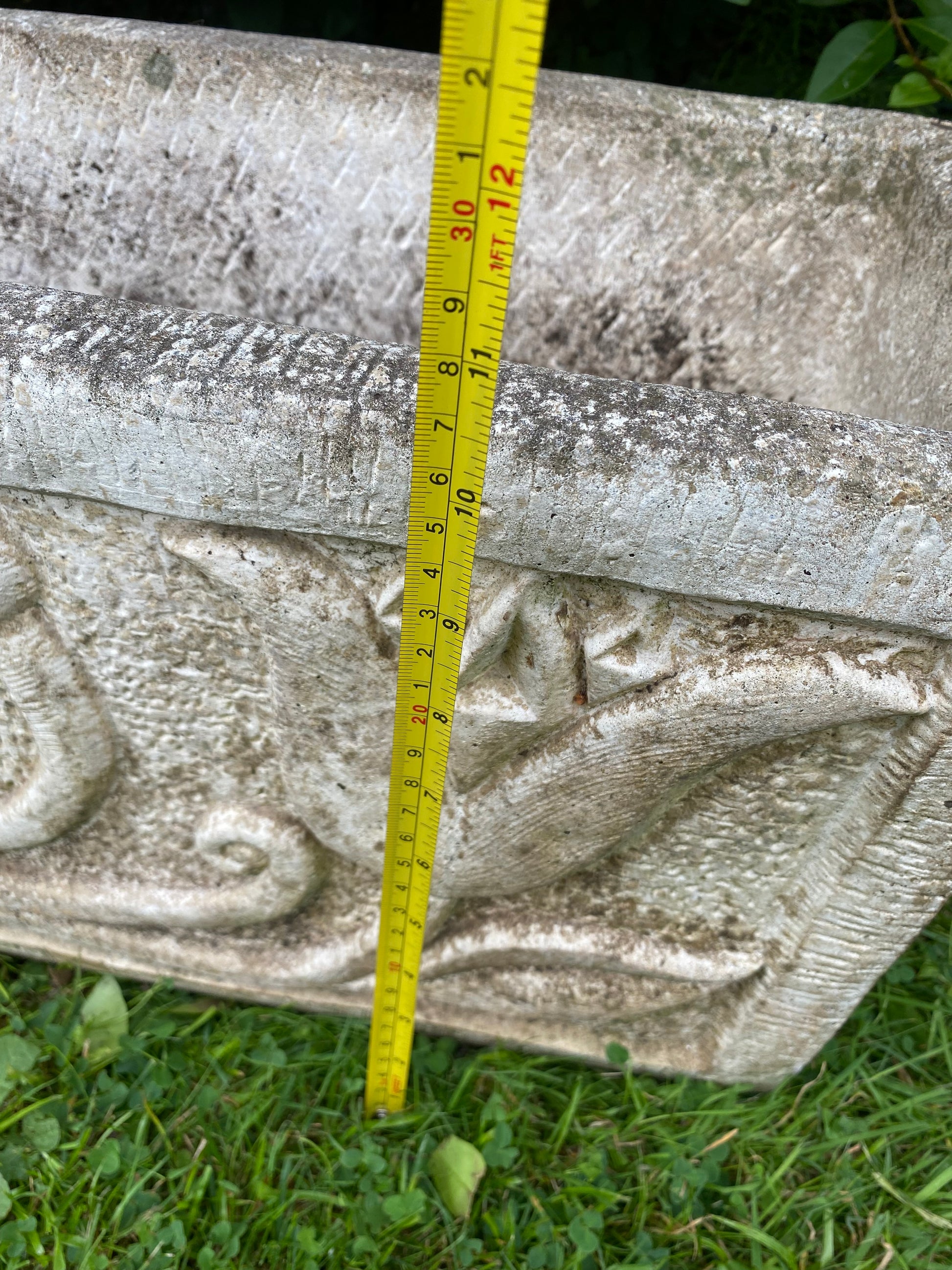 Decorative composite stone planter with a measuring tape for scale on a grassy background