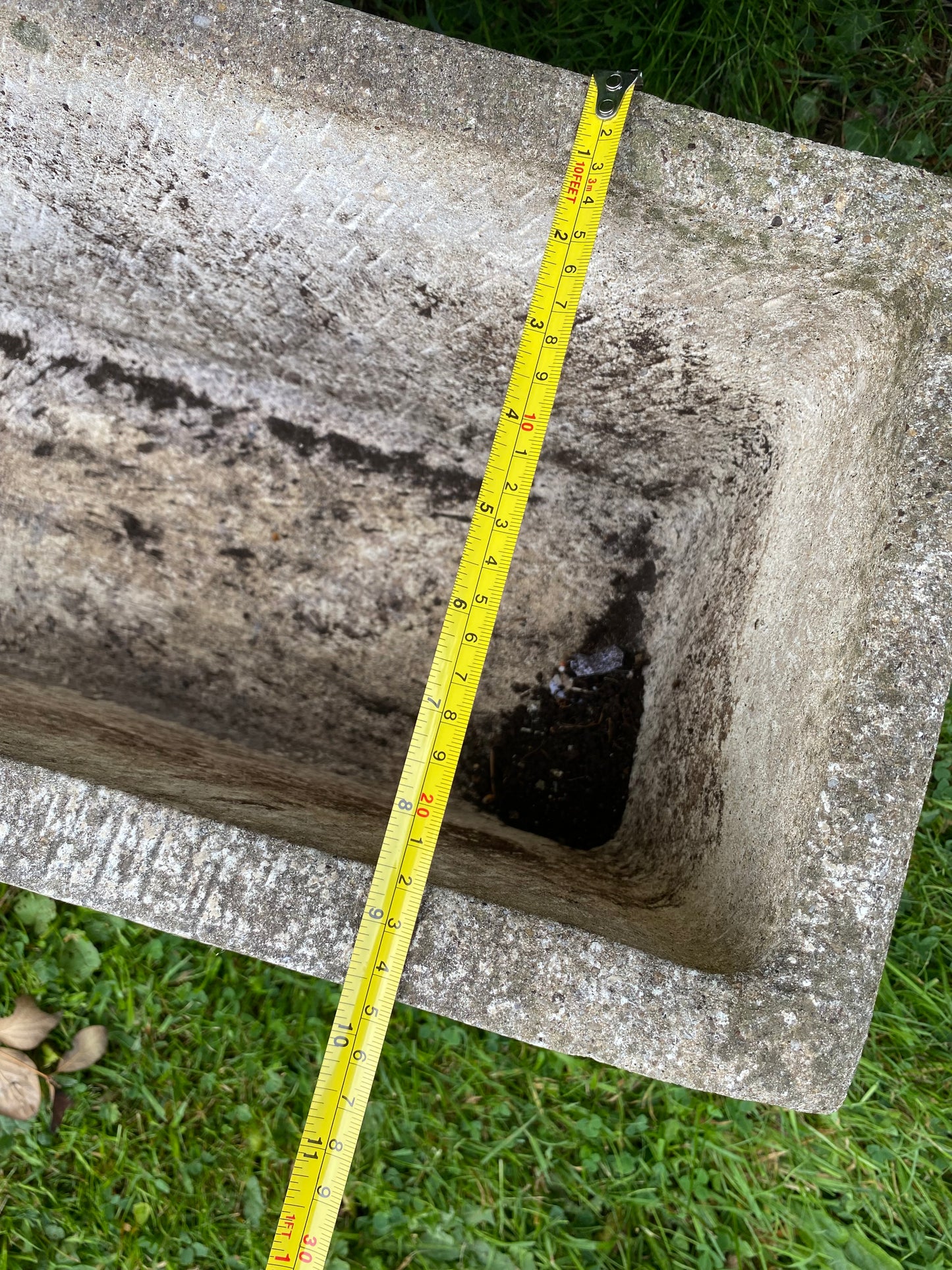 Composite stone planter with a measuring tape indicating dimensions on a grassy background