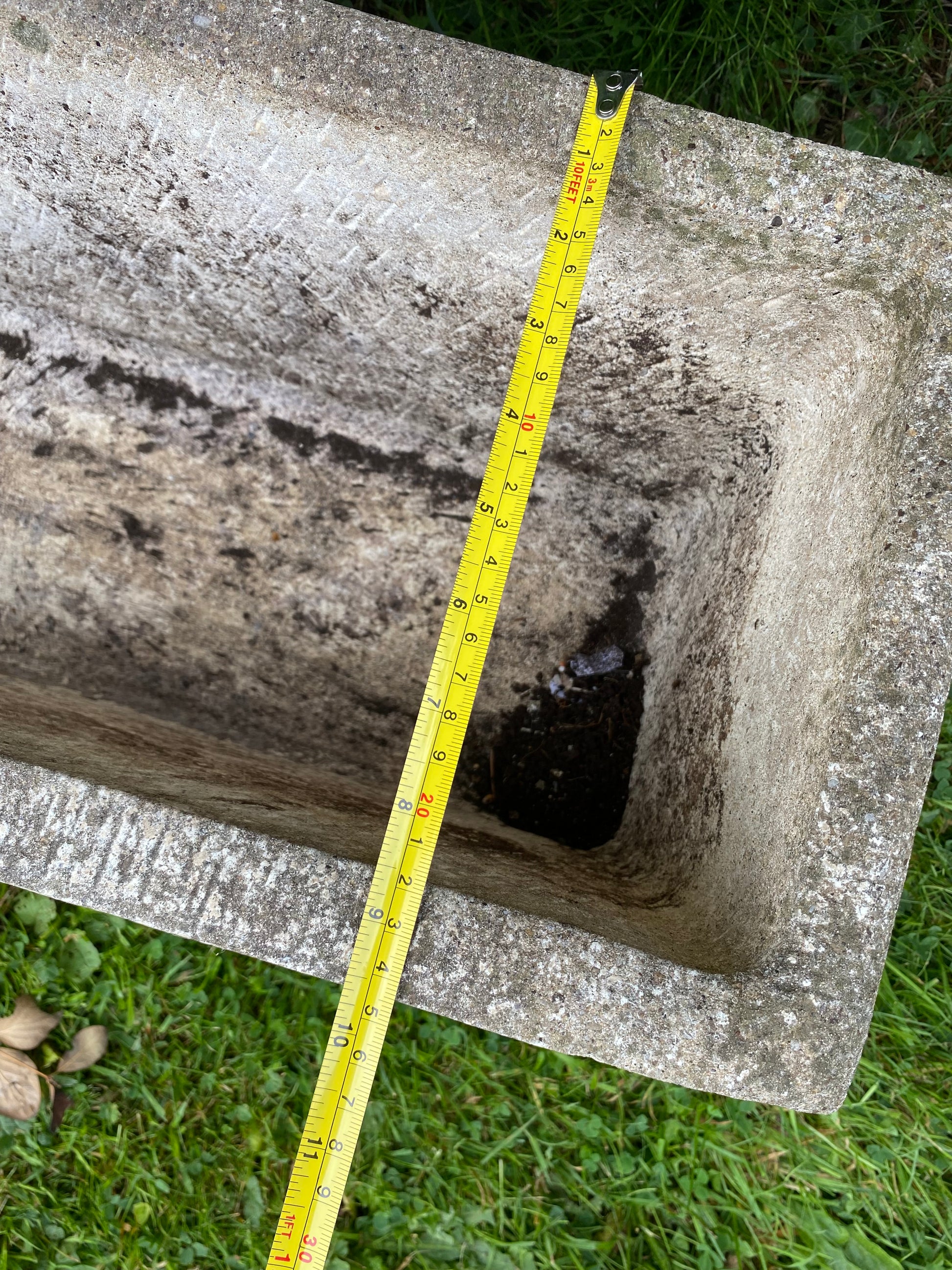 Composite stone planter with a measuring tape indicating dimensions on a grassy background