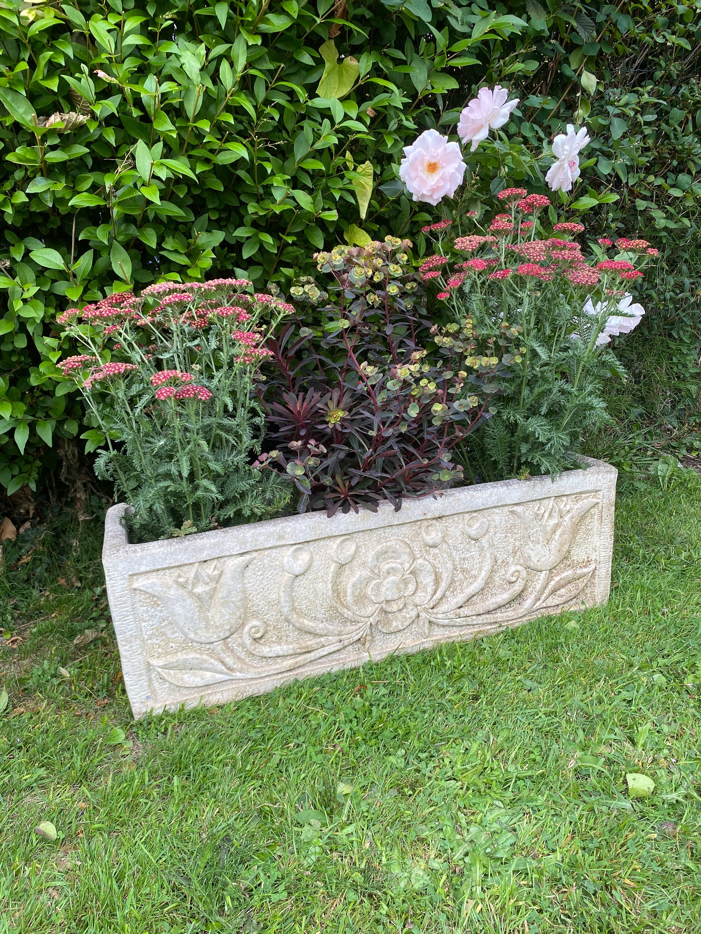 Decorative stone planter in a garden setting with flowers and greenery.