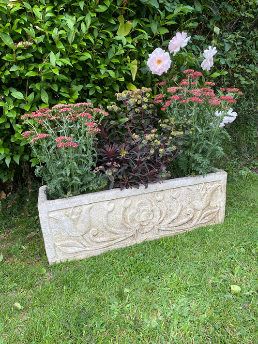 Decorative stone planter in a garden setting with flowers and greenery.