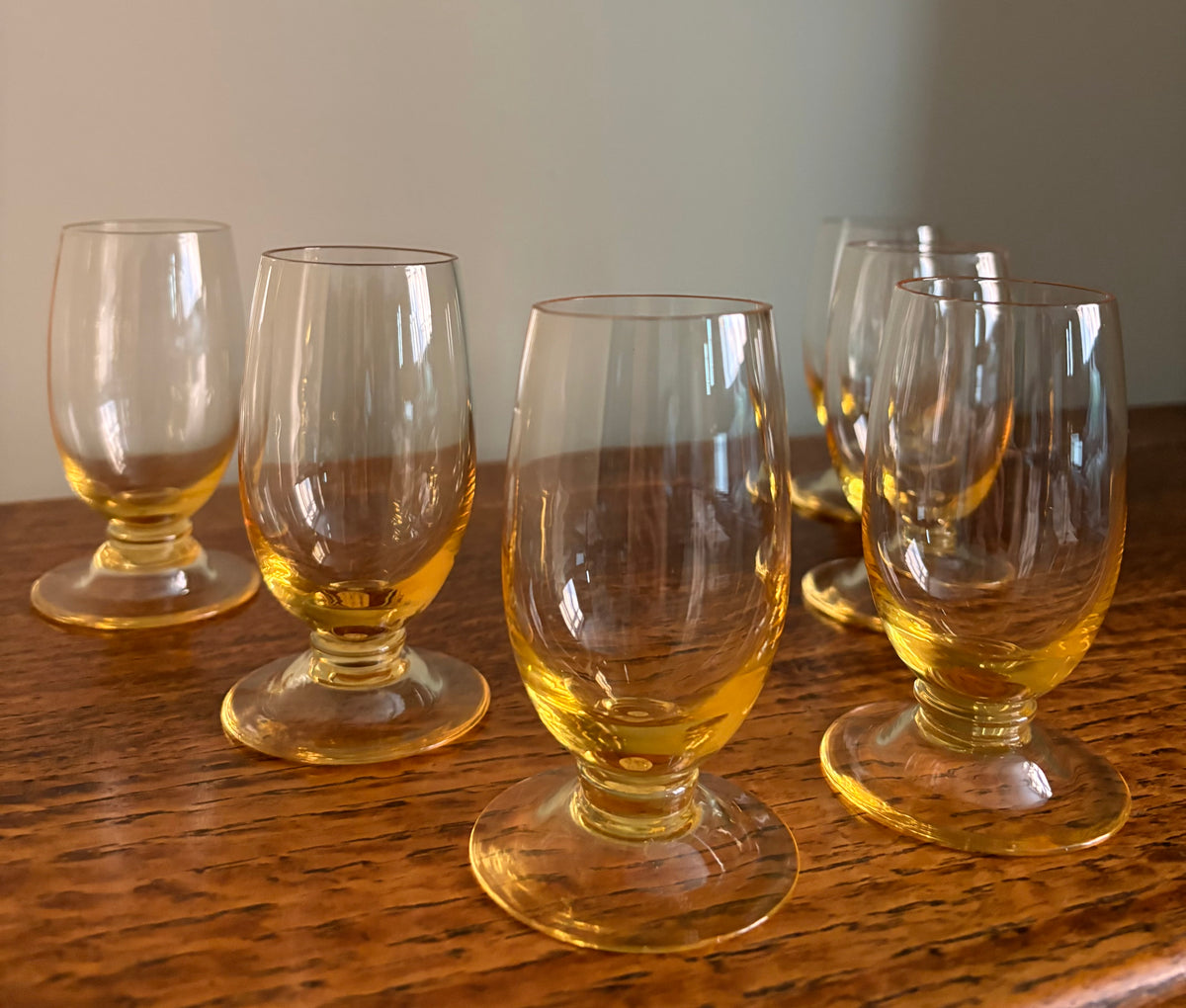Six Whitefriars amber-tinted sherry or port glasses arranged on a wooden tabletop against a plain cream wall.