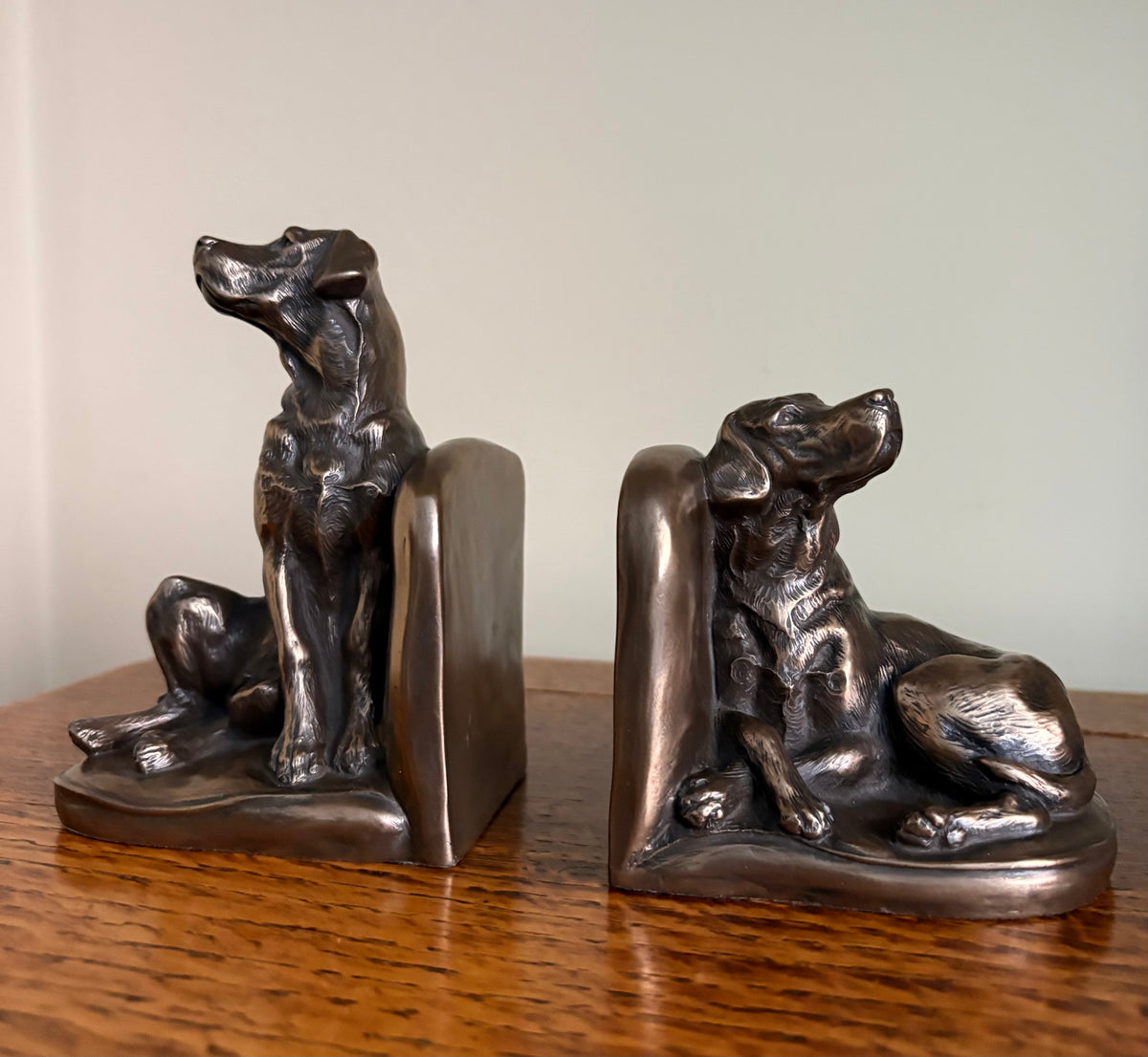 Pair of Genesis Heredities cast resin bronze effect bookends, modelled as Labrador dogs and shaped one seated and one lying down, displayed on a wooden surface against a plain light background. 