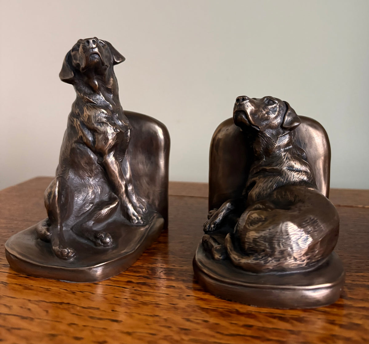 Pair of Genesis Heredities cast resin bronze effect bookends, modelled as Labrador dogs and shaped one seated and one lying down, displayed on a wooden table against a neutral background.